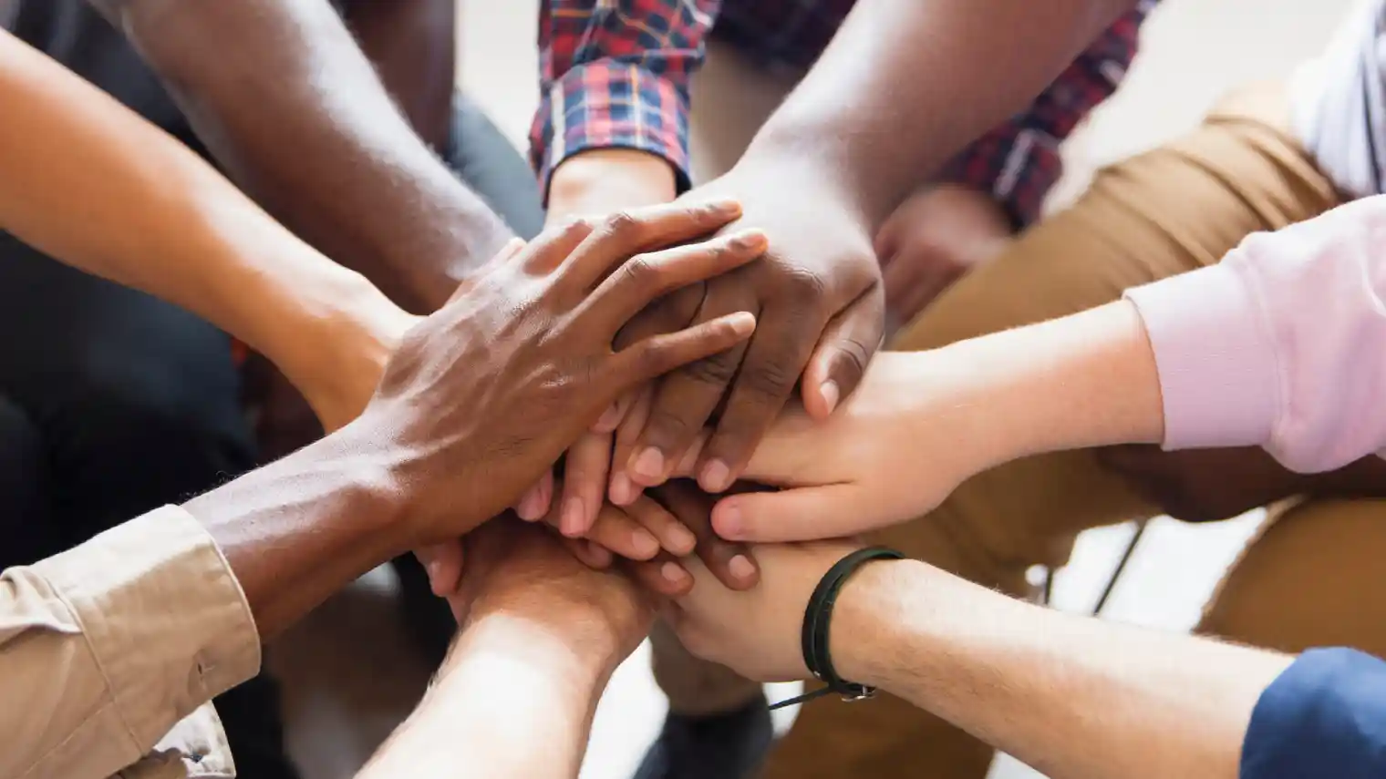 A group of diverse hands come together in a stack, signifying unity, support, and about us at Invigorate.